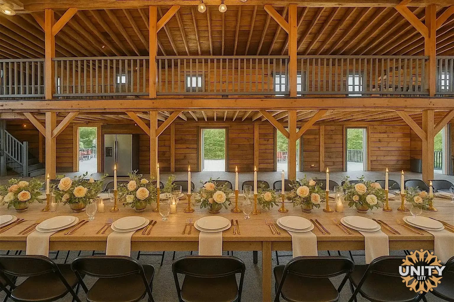 The barn laid for a meal — one long table under a timber frame, candles and roses down the middle