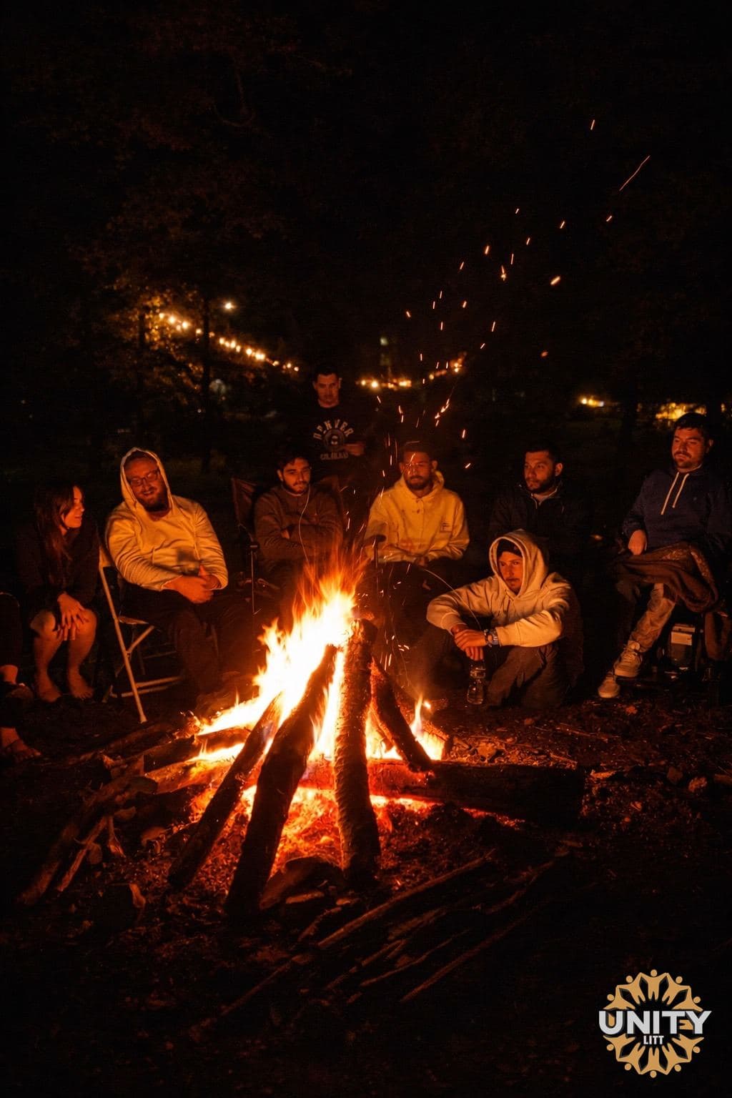 People gathered close around a fire pit at night, faces lit orange