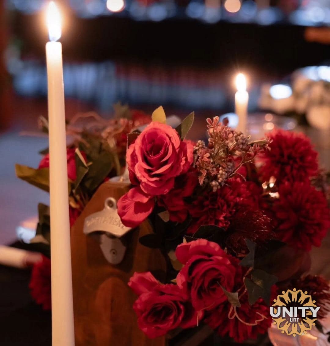 Tall candles burning beside deep red roses on a table
