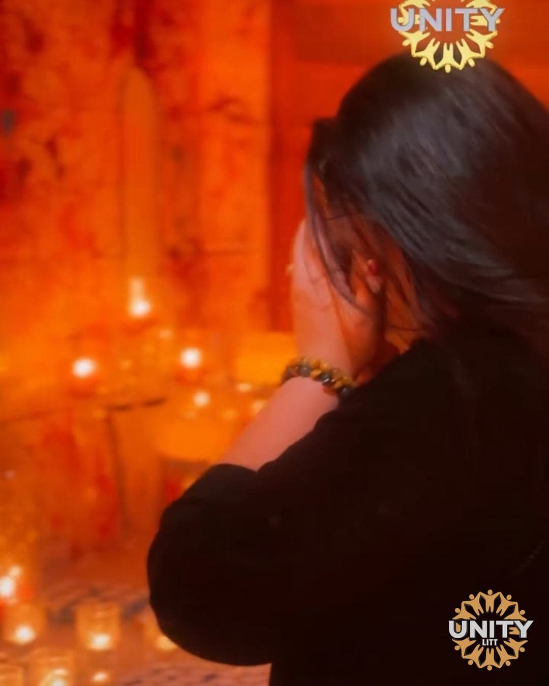 A woman beside a wall of candles, the room glowing orange