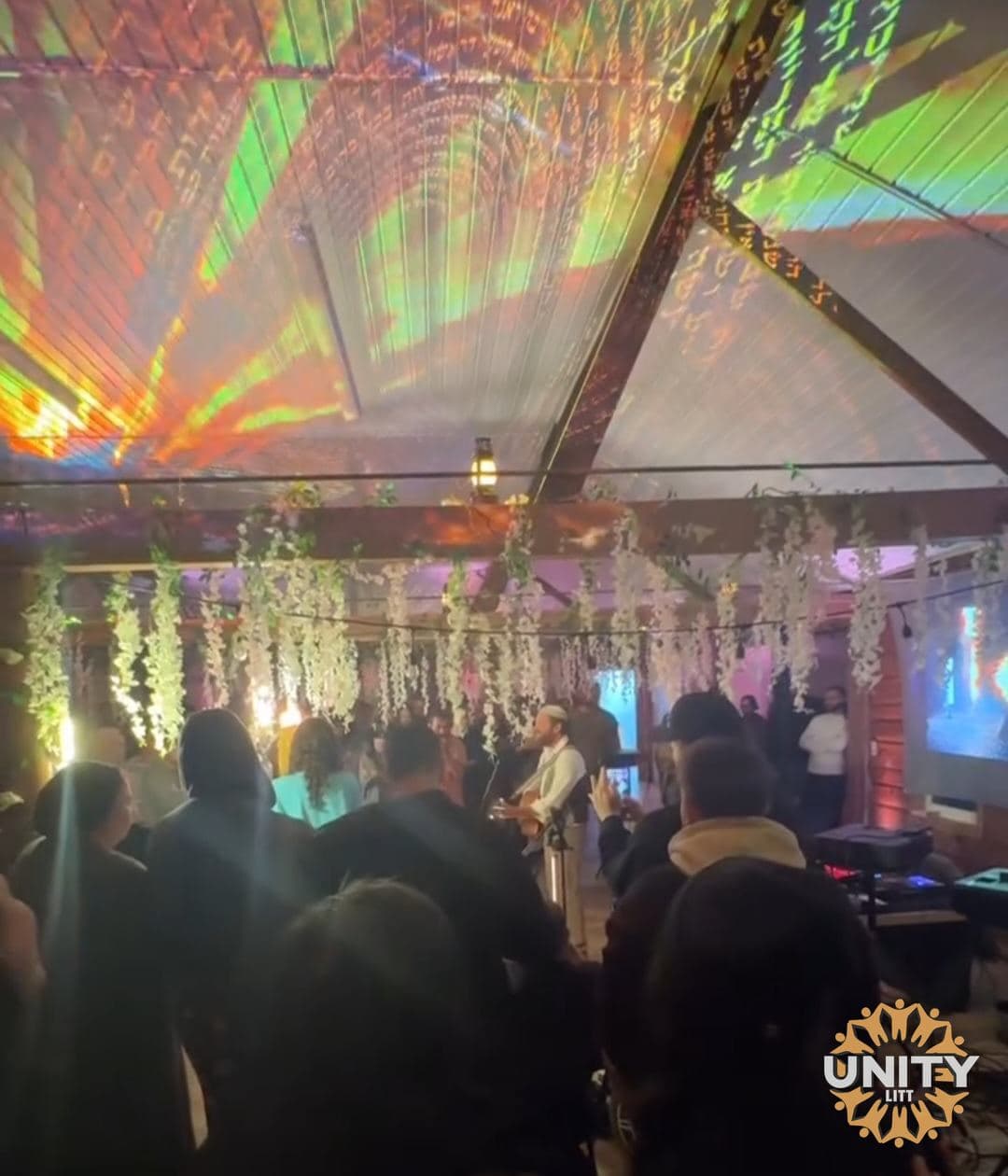 A crowd from behind, coloured light spilling across the ceiling
