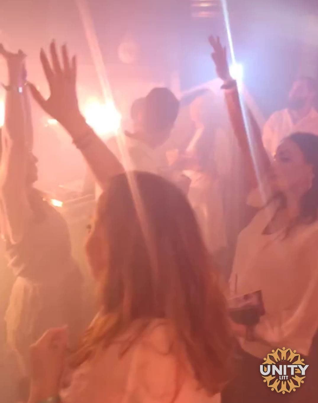 Hands in the air on the dance floor, light cutting through the haze