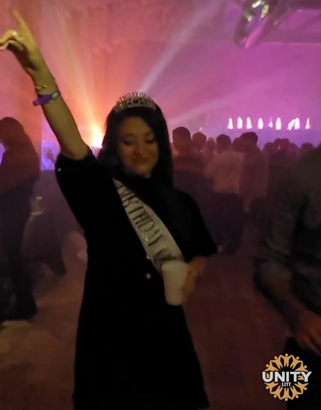 A woman dancing with her arm raised, the room lit pink behind her
