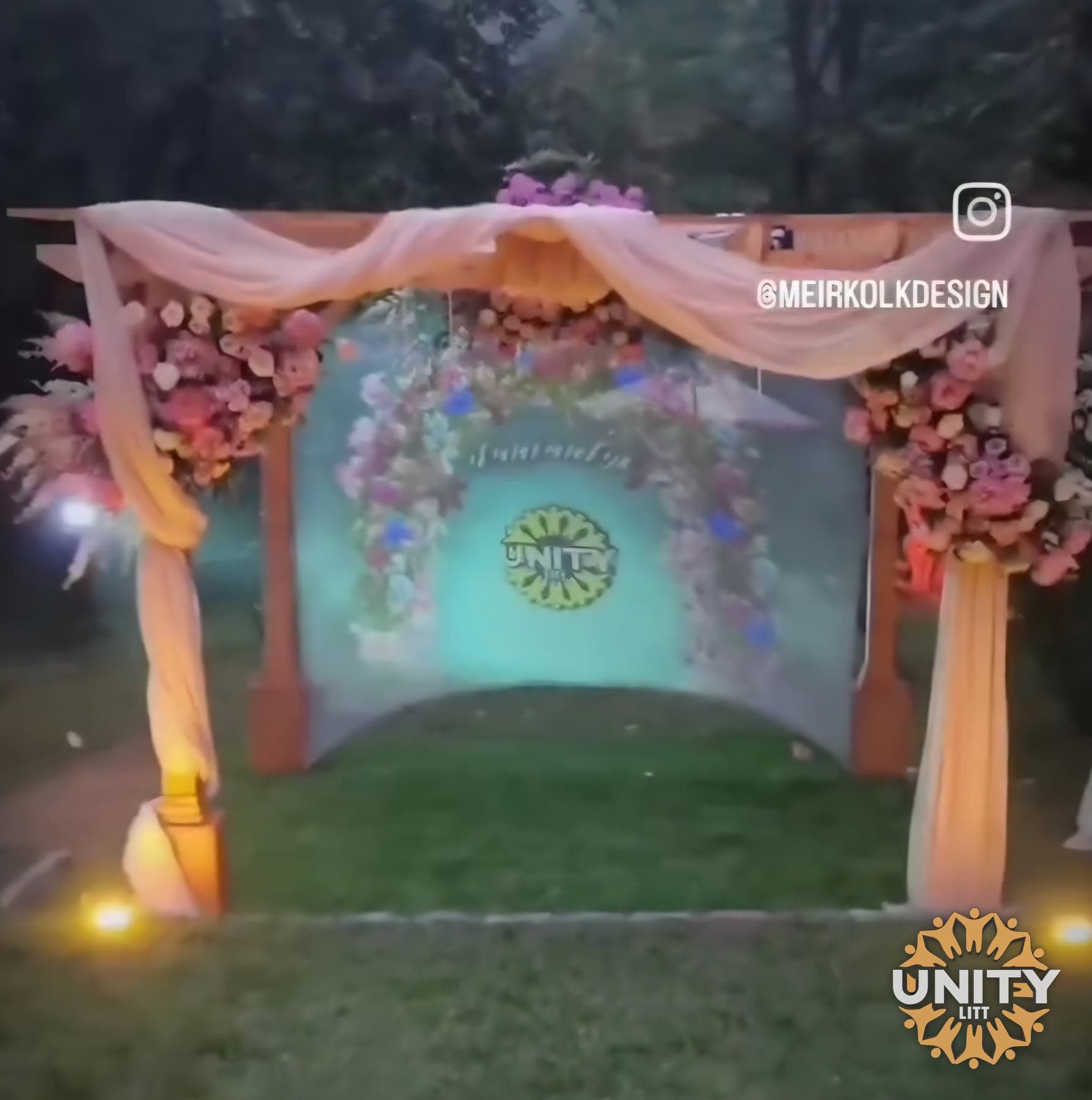 A floral arch set up outdoors with light behind it