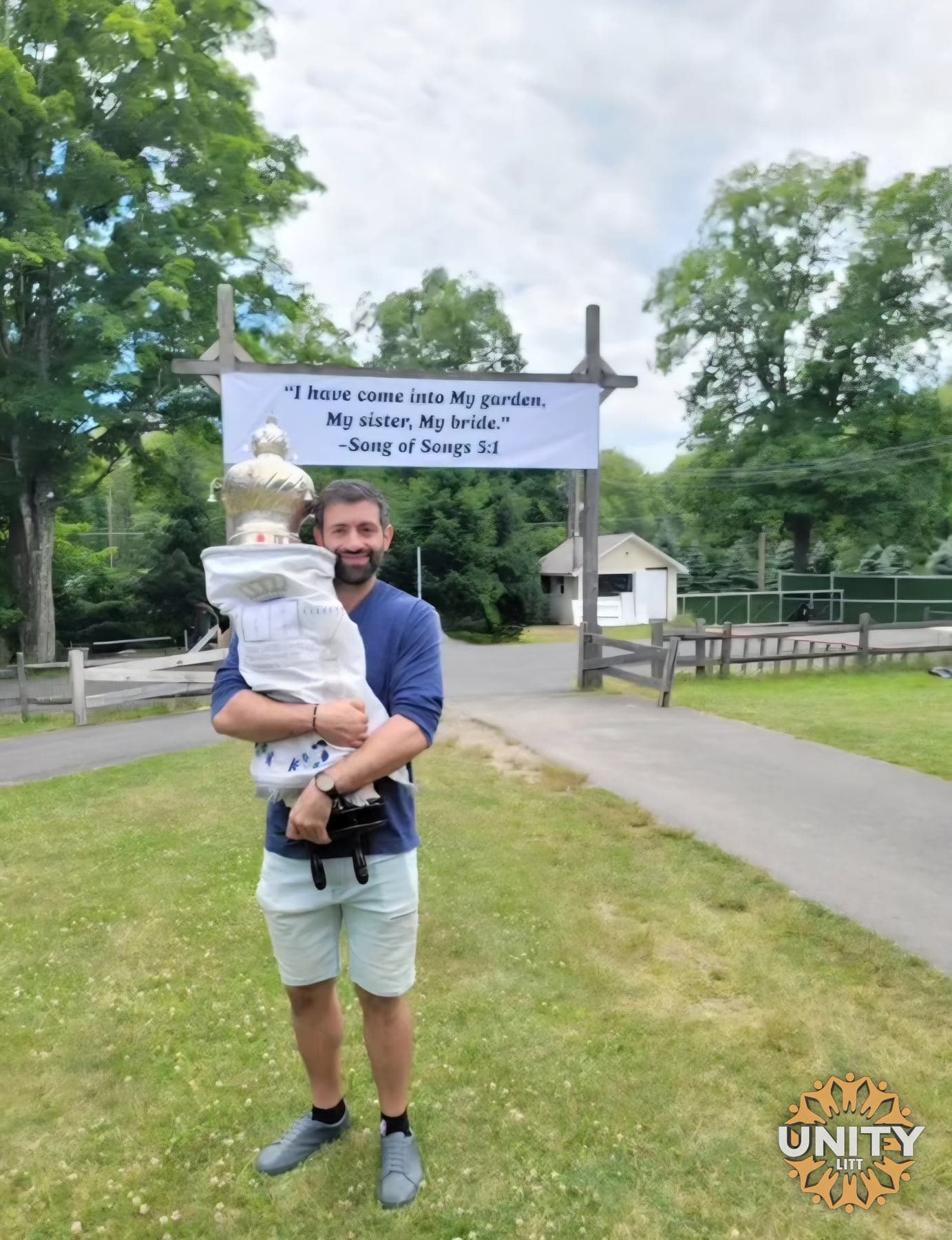 A man carrying a small child past the sign at the entrance to the property