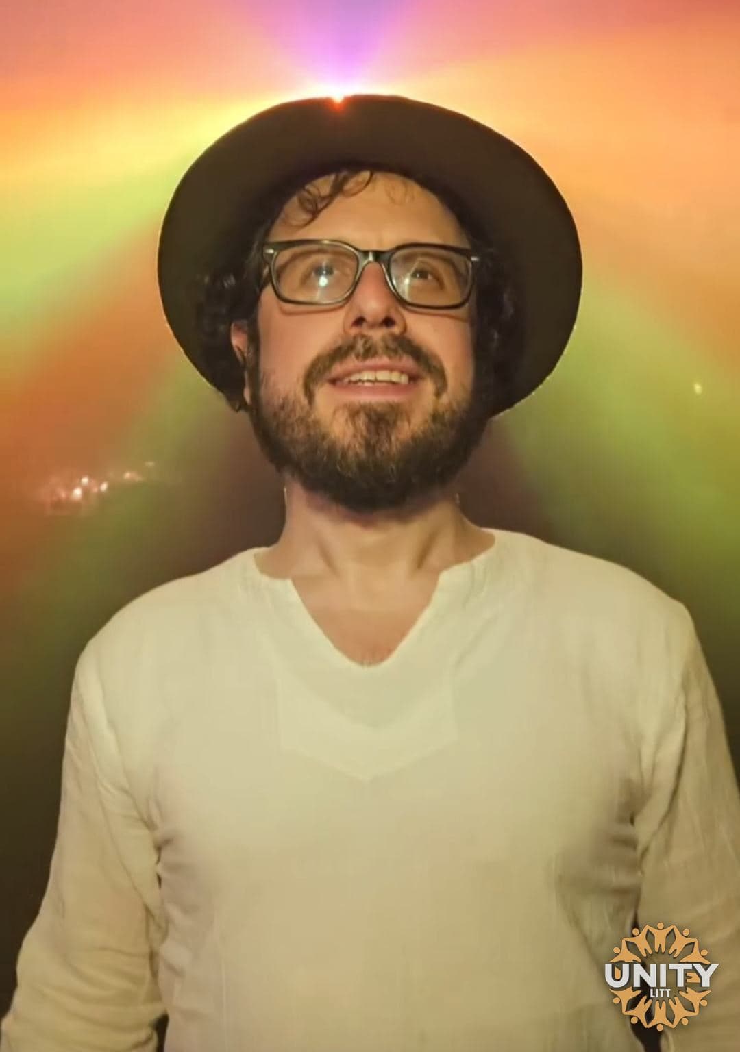 A man in a hat lit by warm light, looking up