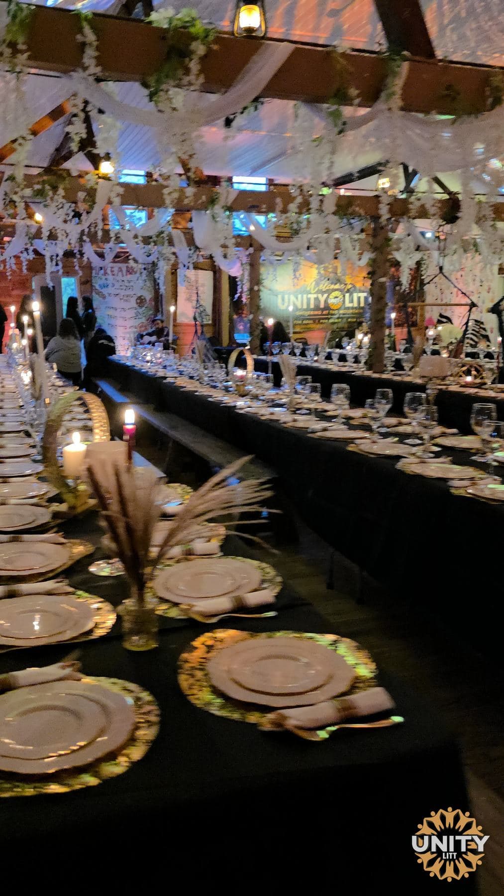 Long tables set for a meal under strings of lights and hanging florals