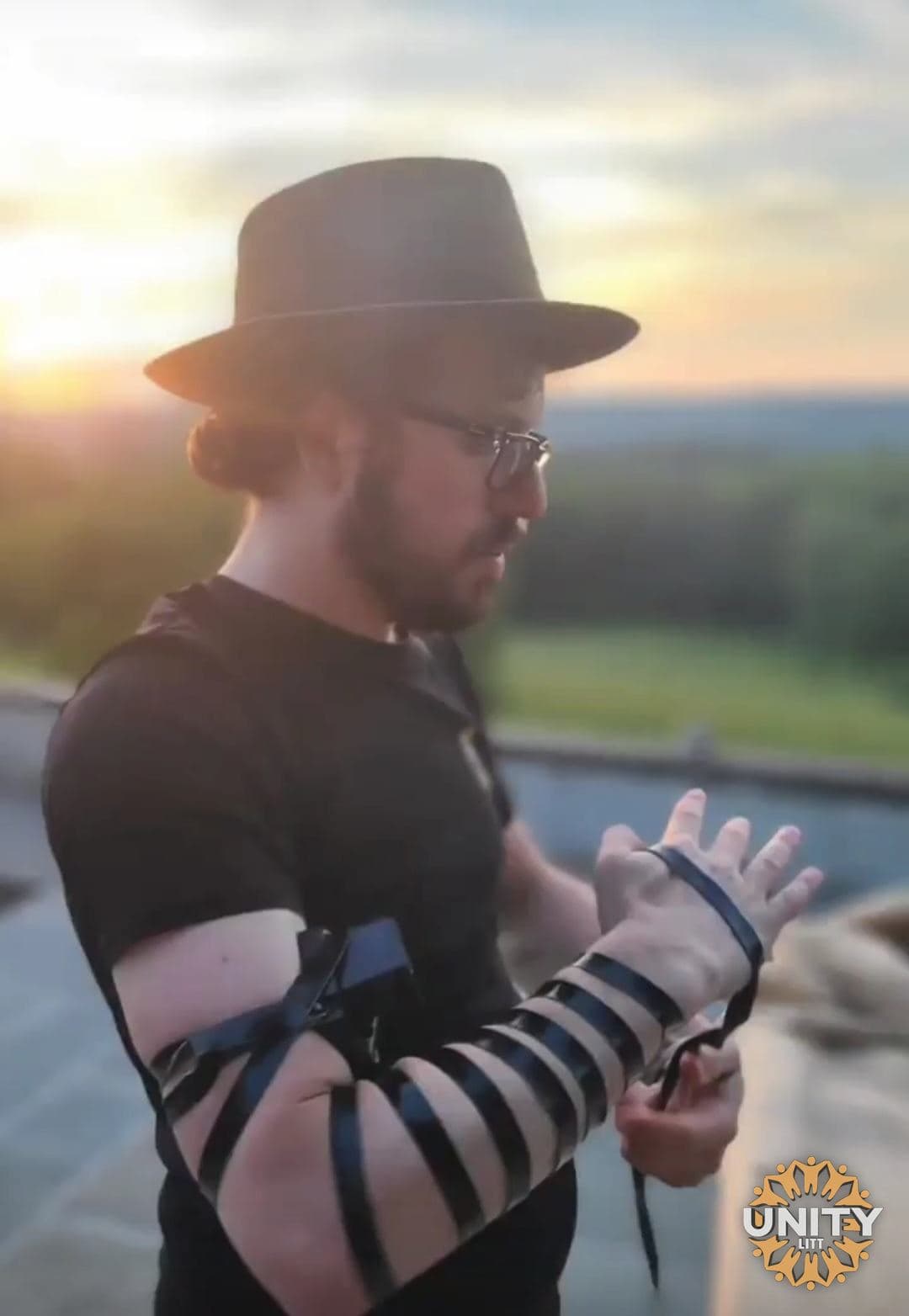 A man putting on tefillin outdoors as the sun comes up