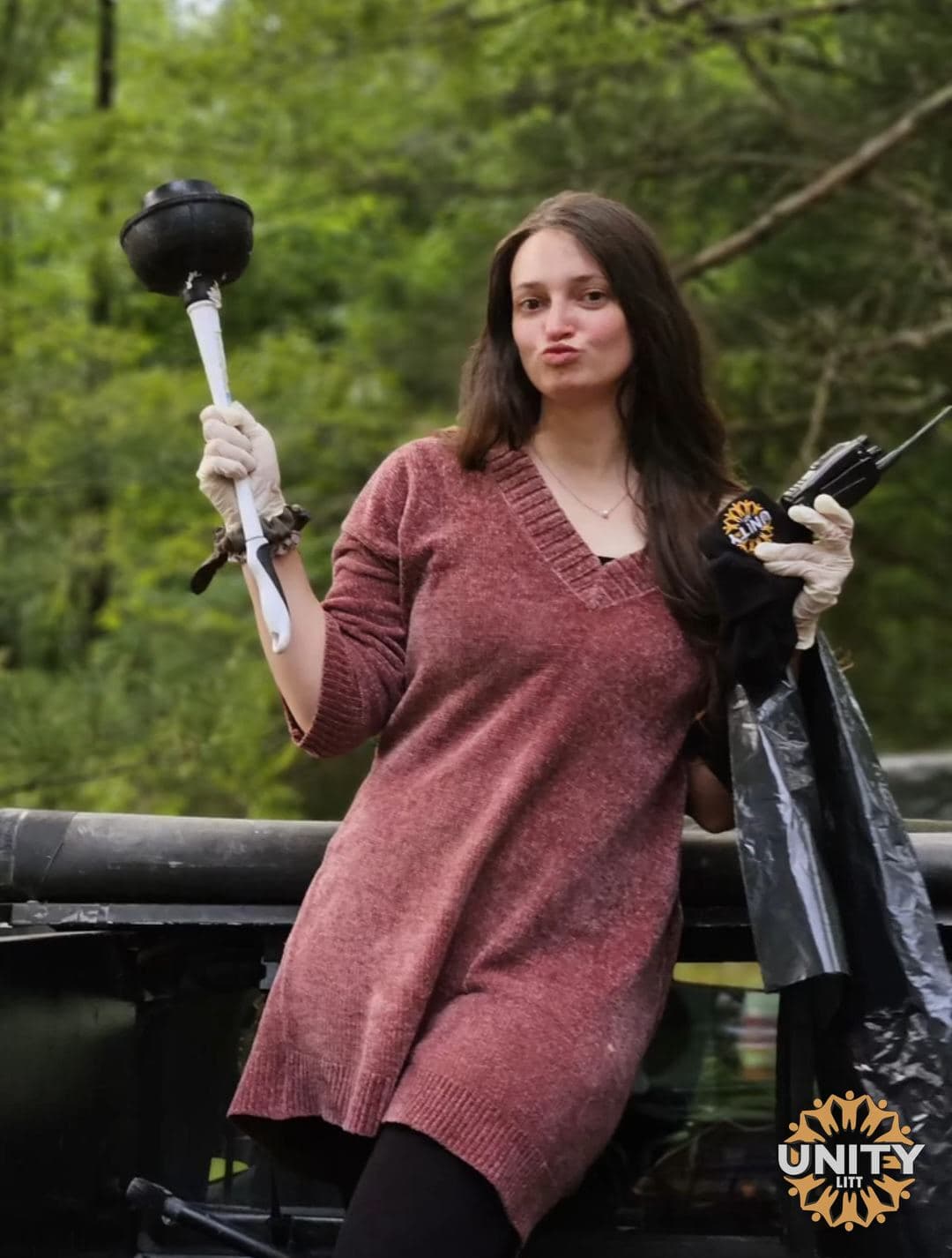 A woman pulling a face while holding up a plunger and a rubbish bag